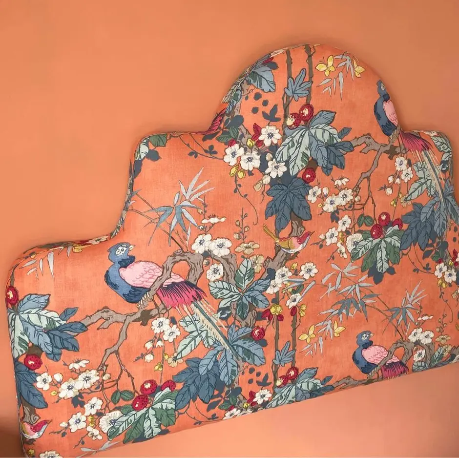A shaped bespoke headboard in a coral chinoiserie of birds, blossom and bamboo