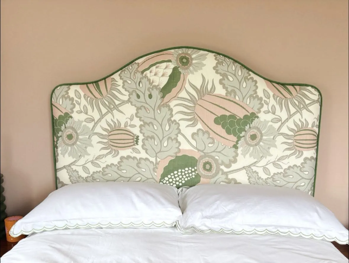 A camel-back headboard in a sage-and-blush botanical linen with green piping