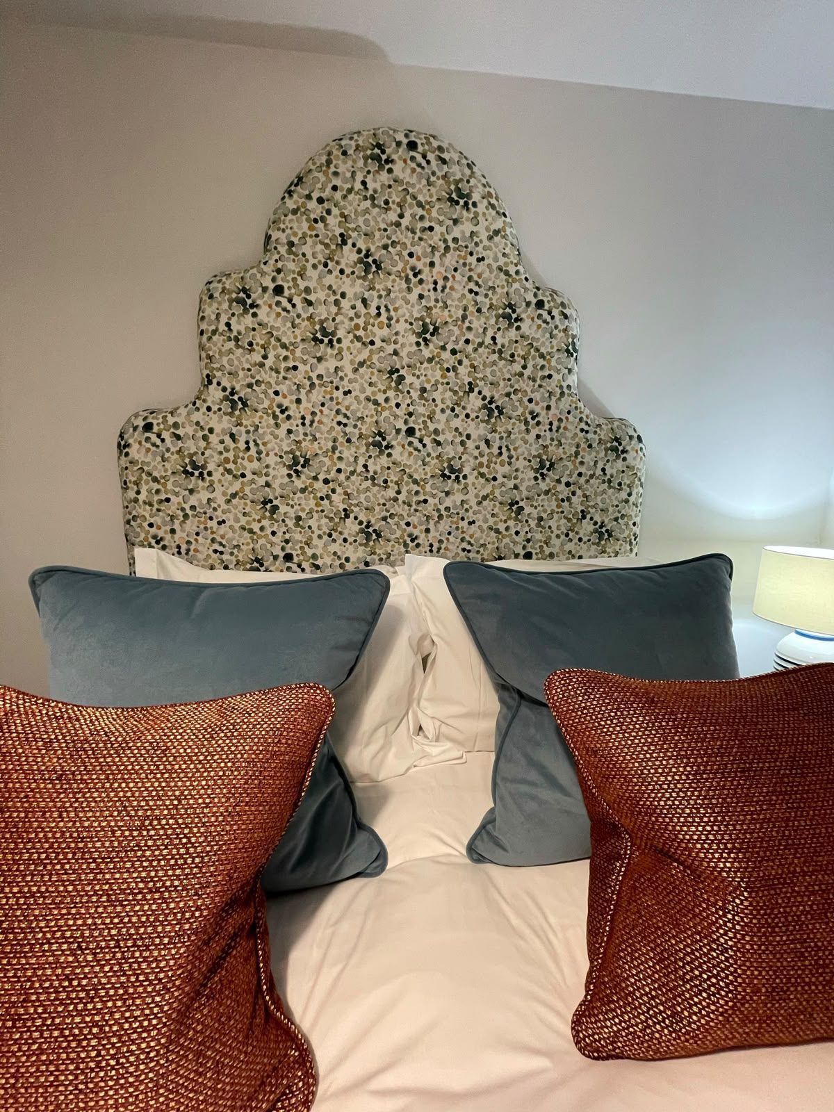 A shaped headboard in a blue botanical print, dressed with rust and grey cushions