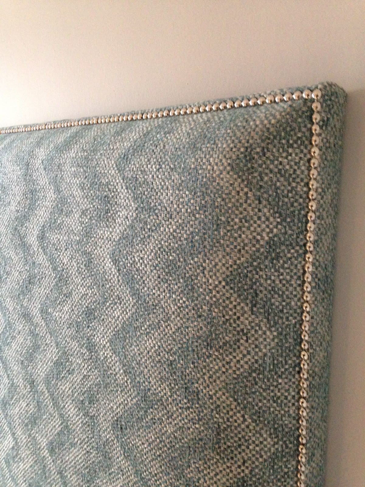 A headboard in a grey chevron weave, finished with a hand-set stud trim