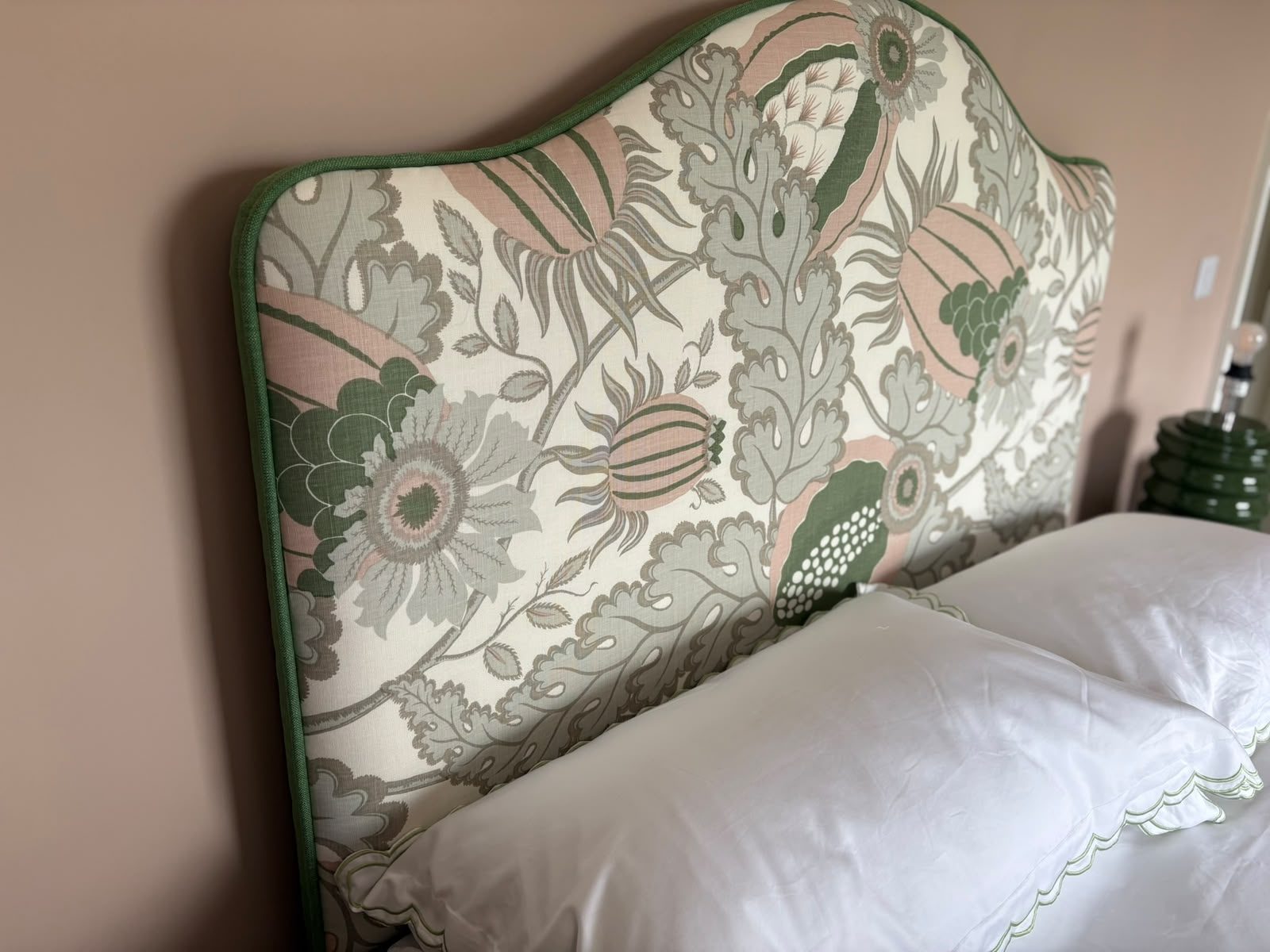 A shaped headboard in a green-and-blush Morris-style floral with contrast piping