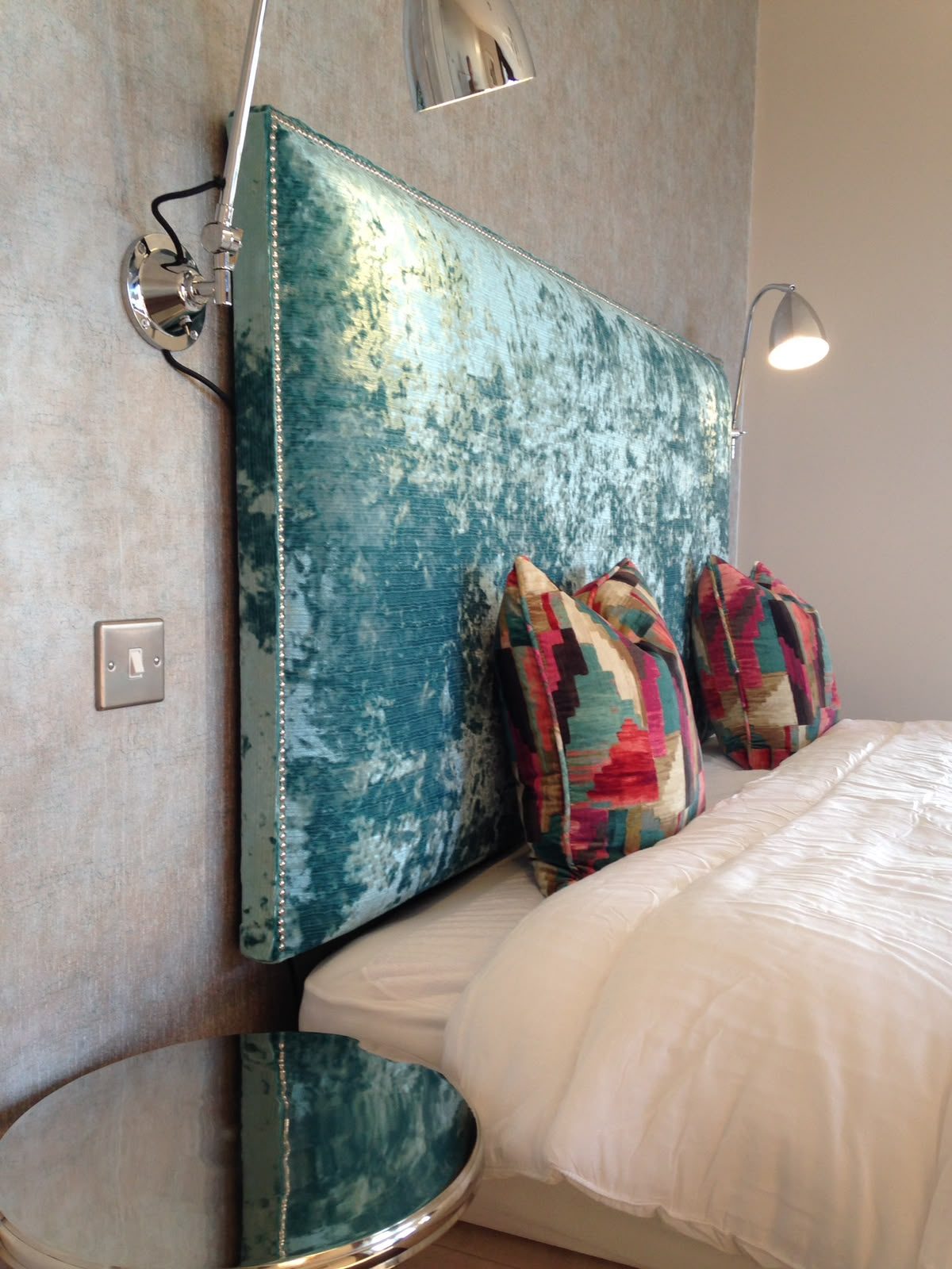 A headboard in a teal peacock chinoiserie, dressed with patterned cushions