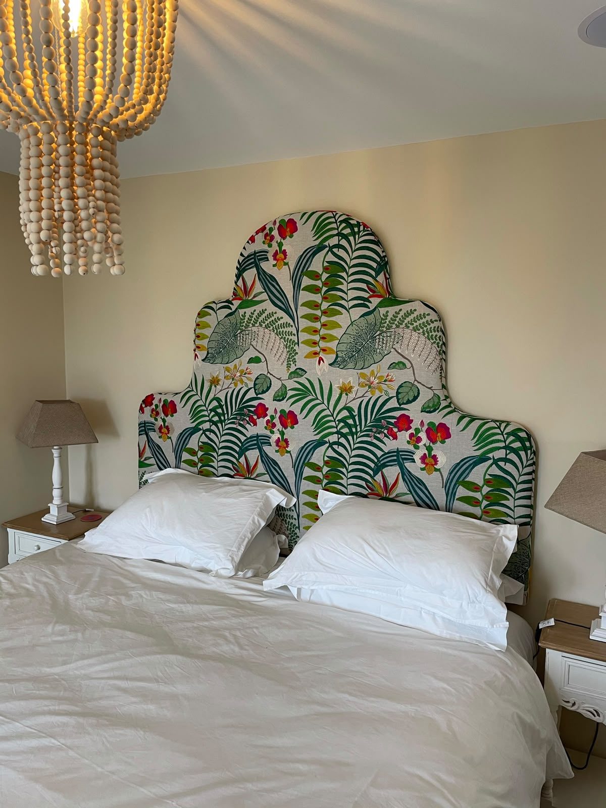 A softly shaped headboard in a bold tropical-floral linen of ferns, birds and blossom