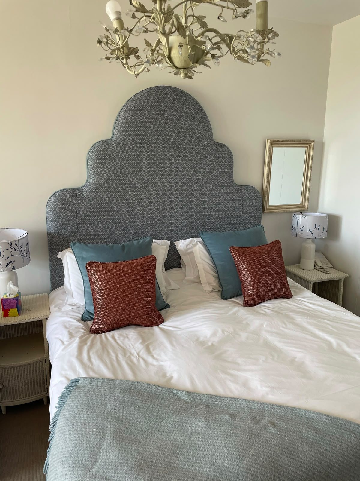 A tall arched headboard in a patterned velvet, with teal and rust cushions