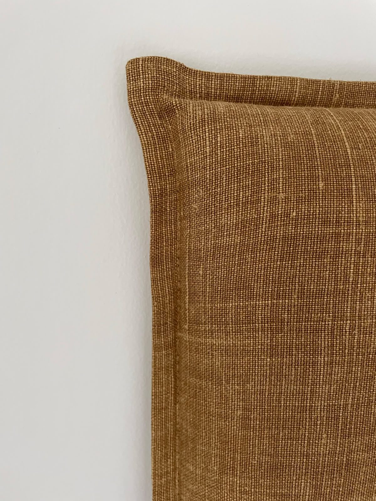 A headboard corner in a natural woven fabric, hand-finished