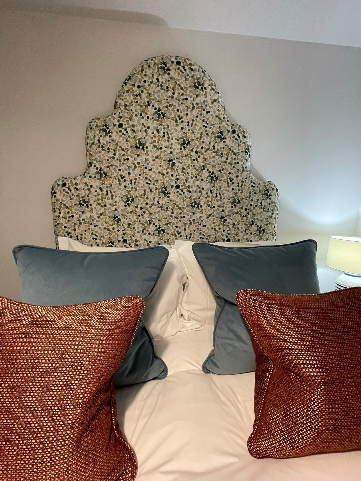 A shaped headboard in a blue botanical print, dressed with rust and grey cushions