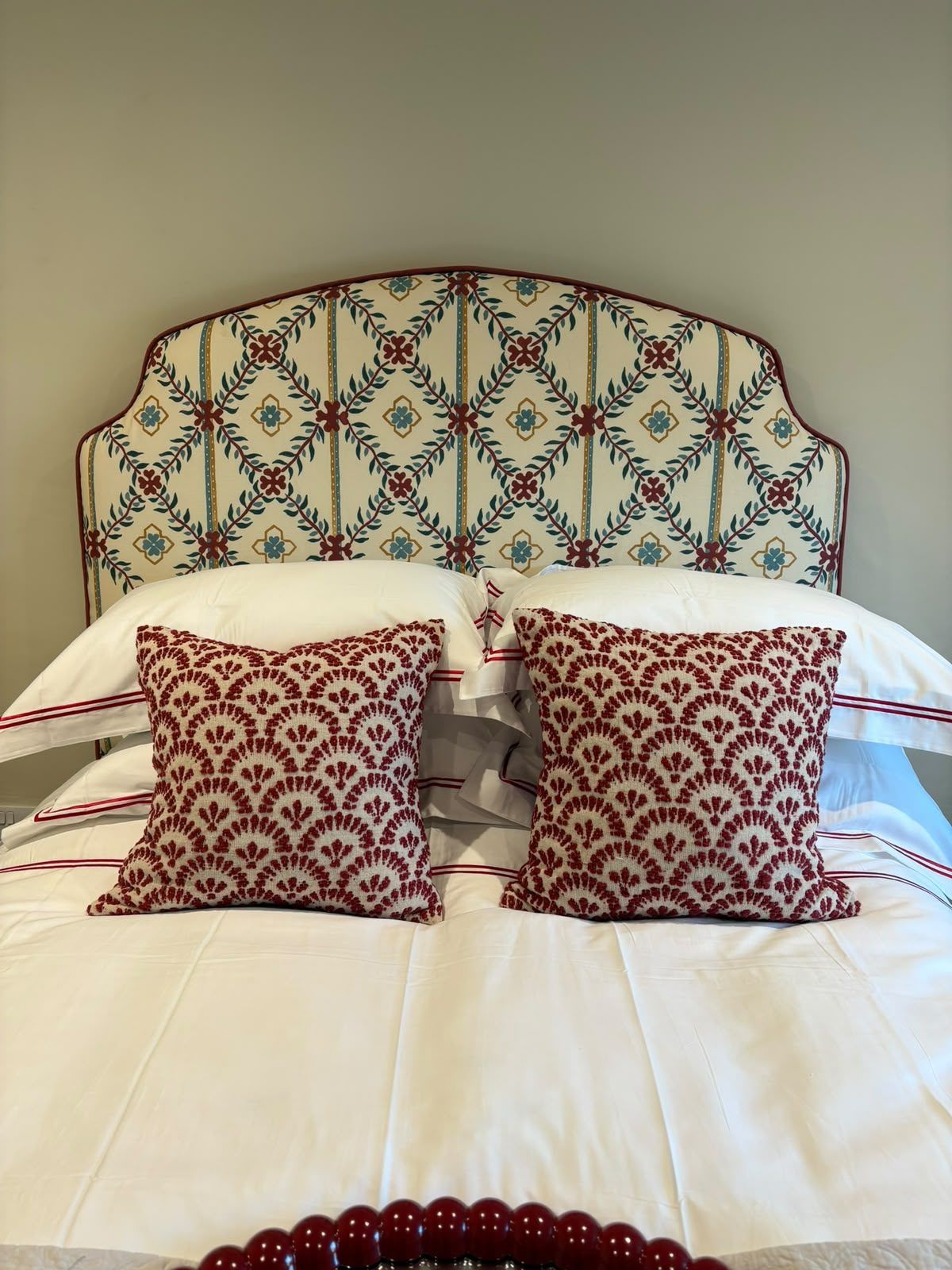 An arched bespoke headboard in a red-and-cream trellis lattice print, above red cushions